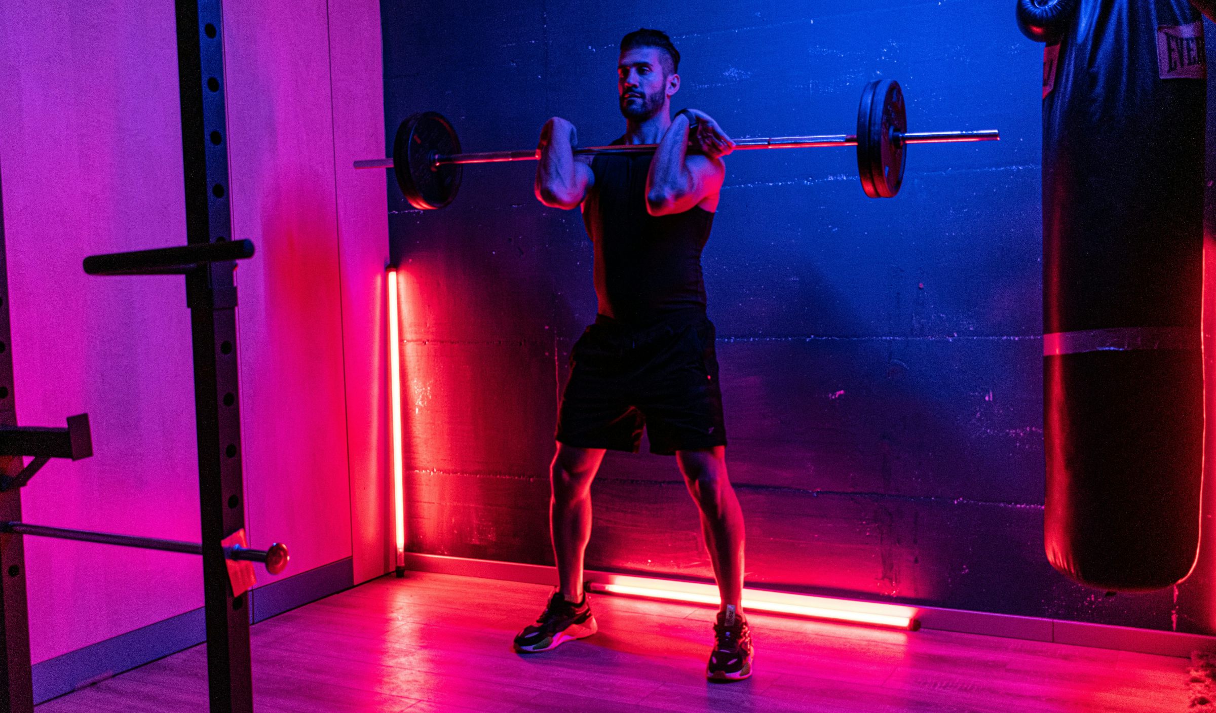 A man holding a barbell in a gym with red and blue lights.