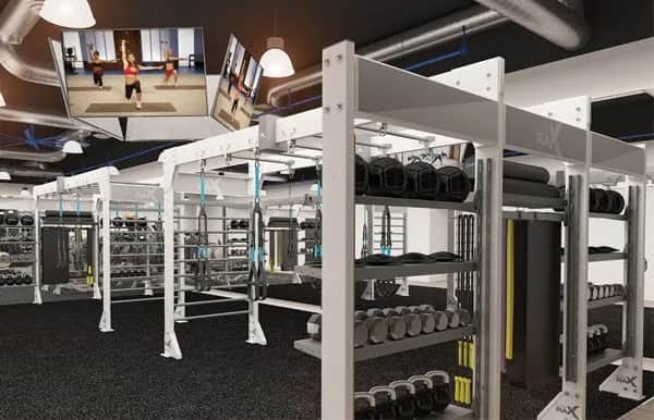 A modern gym with weight racks, dumbbells, and fitness equipment. Large TVs on the ceiling display a workout video. The gym has bright lighting, black flooring, and exposed air ducts.