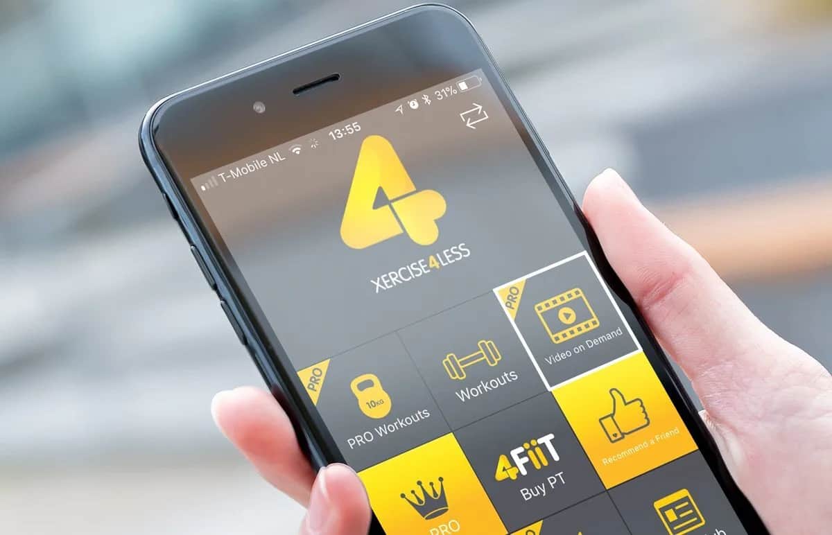 A hand holds a smartphone displaying the 4FLEX4LESS fitness app, showing options like PRO Workouts, Workouts, Video on Demand, Buy PT, and Refer a Friend, with a yellow and gray color scheme.
