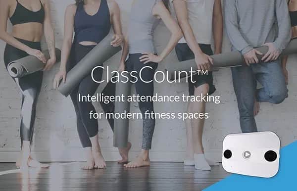 Four people in workout clothes stand against a white brick wall holding yoga mats. Text reads, ClassCount™ Intelligent attendance tracking for modern fitness spaces. A white device appears in the bottom right corner.