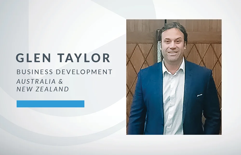 A man in a dark suit and white shirt stands smiling in front of wooden doors. Text beside him reads: Glen Taylor, Business Development, Australia & New Zealand, on a light, geometric background.