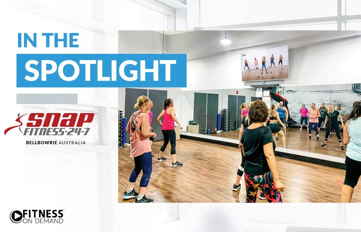 A group fitness class with women exercising in a bright studio with wooden floors and large mirrors at Snap Fitness 24-7 Bellbowrie, Australia. The text reads In the Spotlight and displays the Snap Fitness and Fitness On Demand logos.