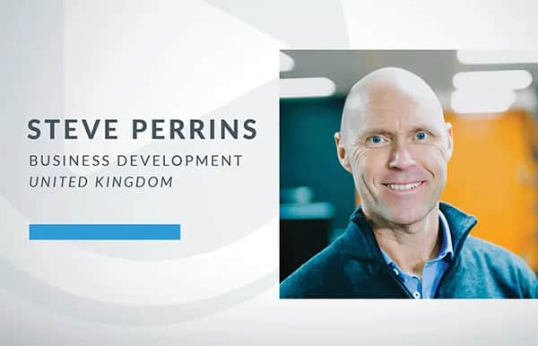A professional profile image featuring Steve Perrins, labeled as working in business development in the United Kingdom, standing indoors and smiling at the camera.