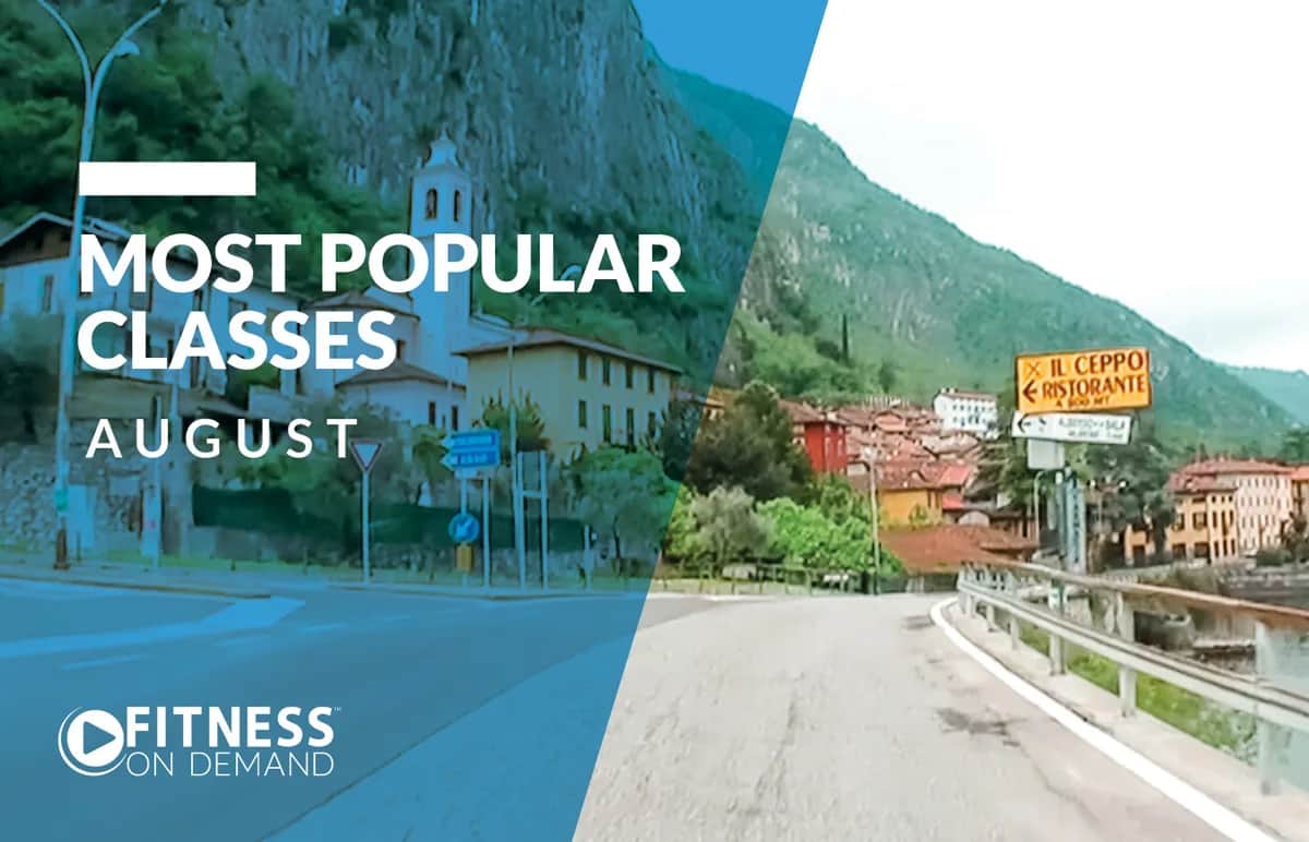 A scenic road winds through a mountainous village with a church and houses. Text reads Most Popular Classes August and Fitness On Demand. A yellow sign ahead points to Il Ceppo Ristorante.