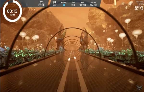 A futuristic, tunnel-like pathway stretches forward through a surreal landscape with glowing orange light, lush plants, and large rock formations. On-screen cycling stats are displayed at the top and left sides of the image.