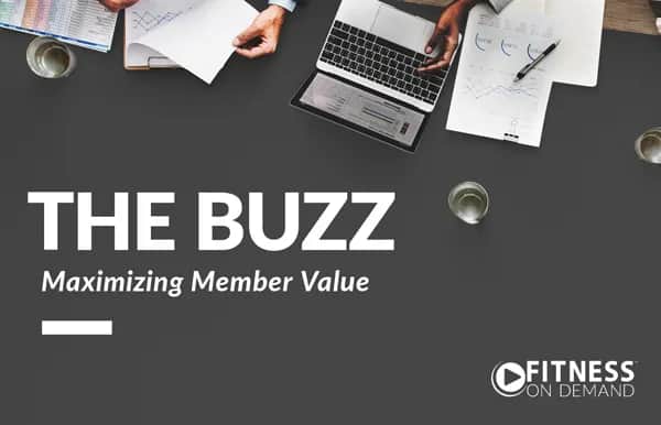 A business meeting setup with people working on documents and a laptop, viewed from above. Text reads THE BUZZ Maximizing Member Value with the Fitness On Demand logo in the corner.