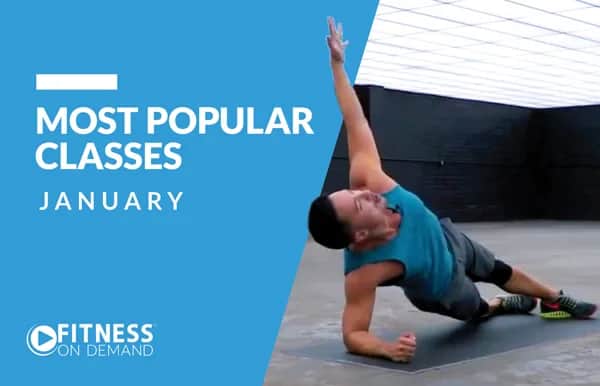 A man in workout clothes performs a side plank with one arm raised in a spacious indoor gym. Text on the left reads Most Popular Classes January and Fitness On Demand.