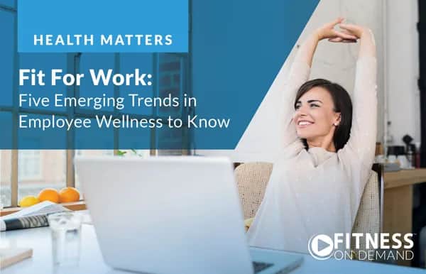 A smiling woman stretches at her desk in a bright office. Text on the image reads: Fit For Work: Five Emerging Trends in Employee Wellness to Know. The Fitness On Demand logo appears in the bottom right corner.
