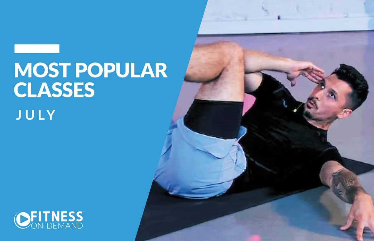 A man wearing a black shirt and light blue shorts does an abdominal exercise on a mat. Text reads Most Popular Classes July and Fitness On Demand on a blue background.