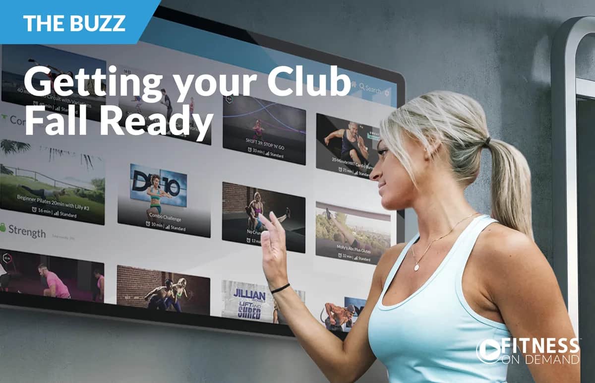 A woman in athletic wear uses a large touchscreen display showing fitness class options, with the text “Getting your Club Fall Ready” and “FITNESS ON DEMAND” in the corner.