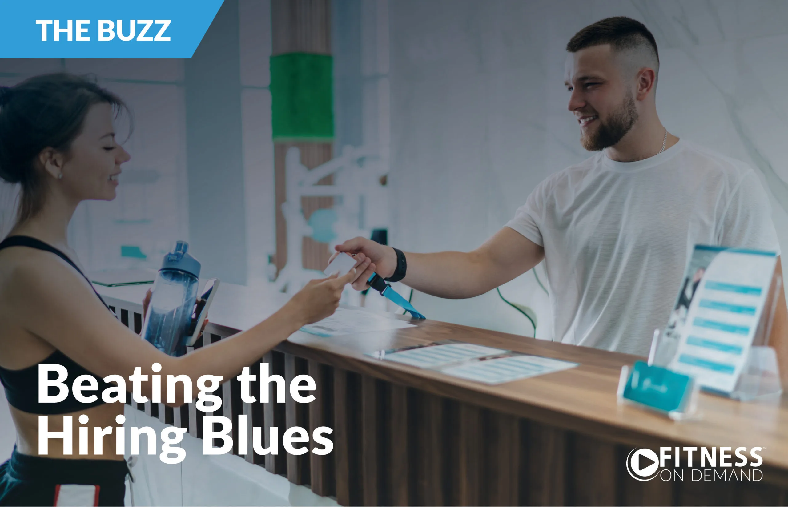 A woman hands a card to a smiling man at a gym reception desk. Text reads The Buzz and Beating the Hiring Blues. Fitness On Demand logo is in the bottom right corner.