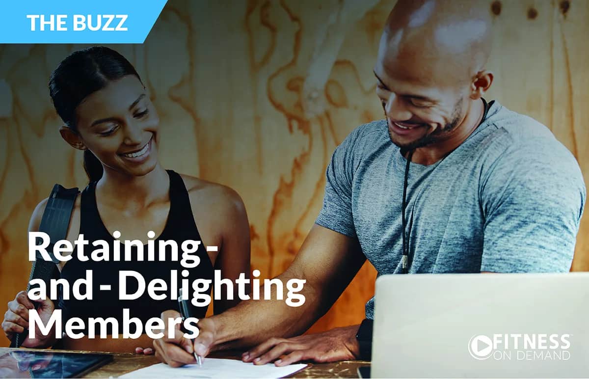 A smiling woman and man sit together at a table, looking at a laptop and papers. Text on image reads: THE BUZZ: Retaining and Delighting Members. FITNESS ON DEMAND.