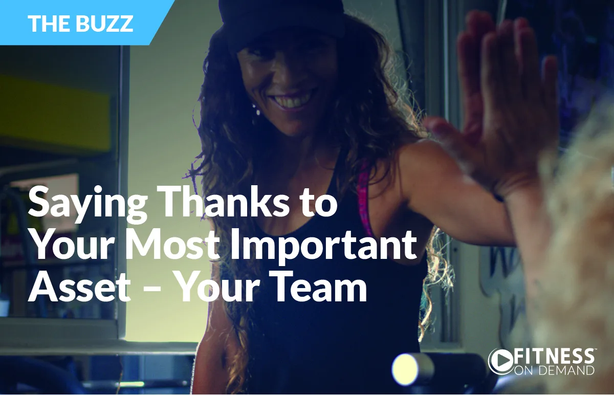 A smiling woman in athletic wear gives a high-five, with text overlay: Saying Thanks to Your Most Important Asset – Your Team. The Fitness On Demand logo is in the bottom right, and THE BUZZ banner is at the top left.