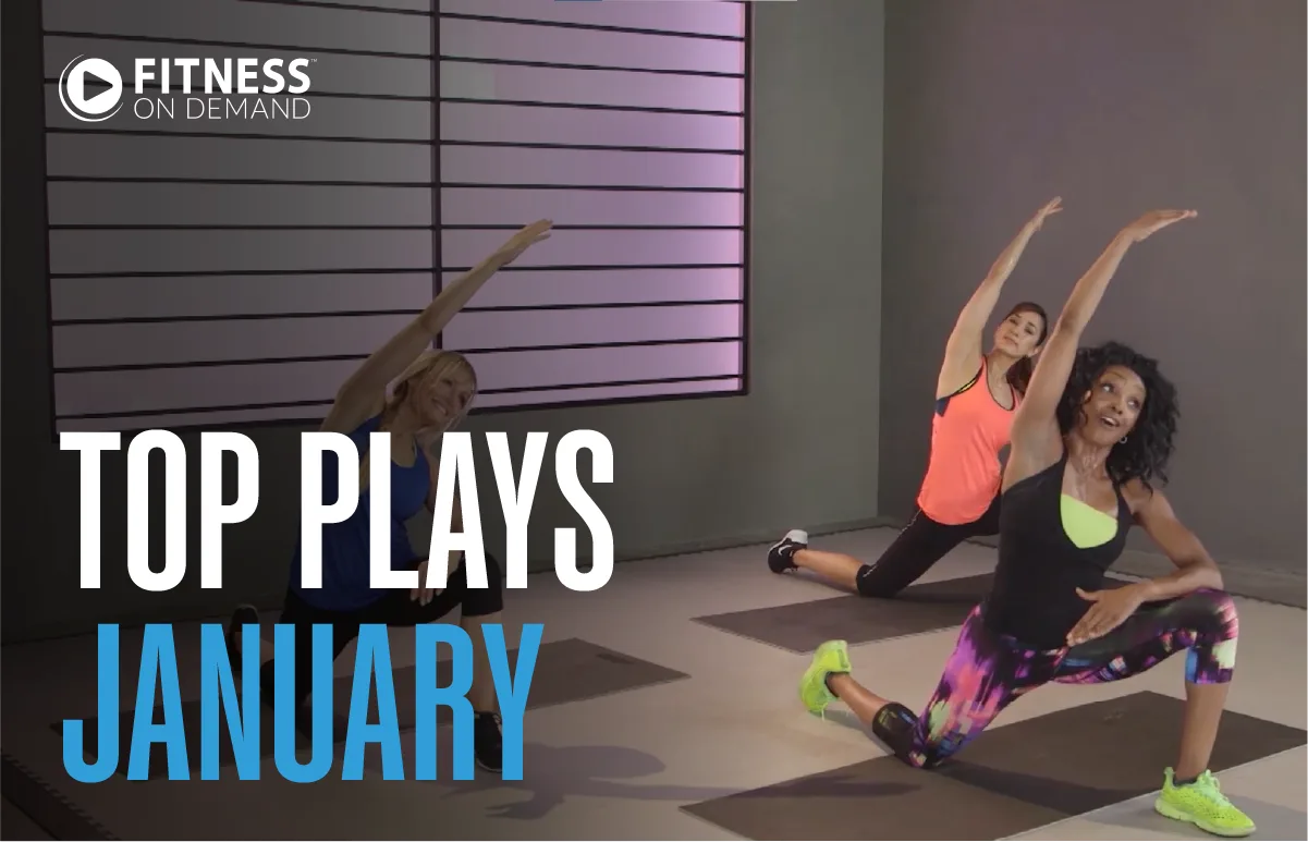Three women in athletic wear do side stretches on yoga mats in a fitness studio. Text reads Fitness On Demand. Top Plays January. Light streams in through a large window in the background.