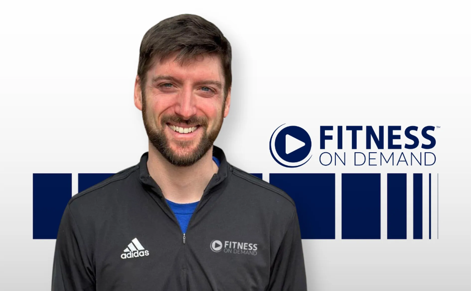 A smiling man with short brown hair and a beard wears a black Fitness On Demand jacket, standing in front of a Fitness On Demand logo and blue geometric shapes on a white background.