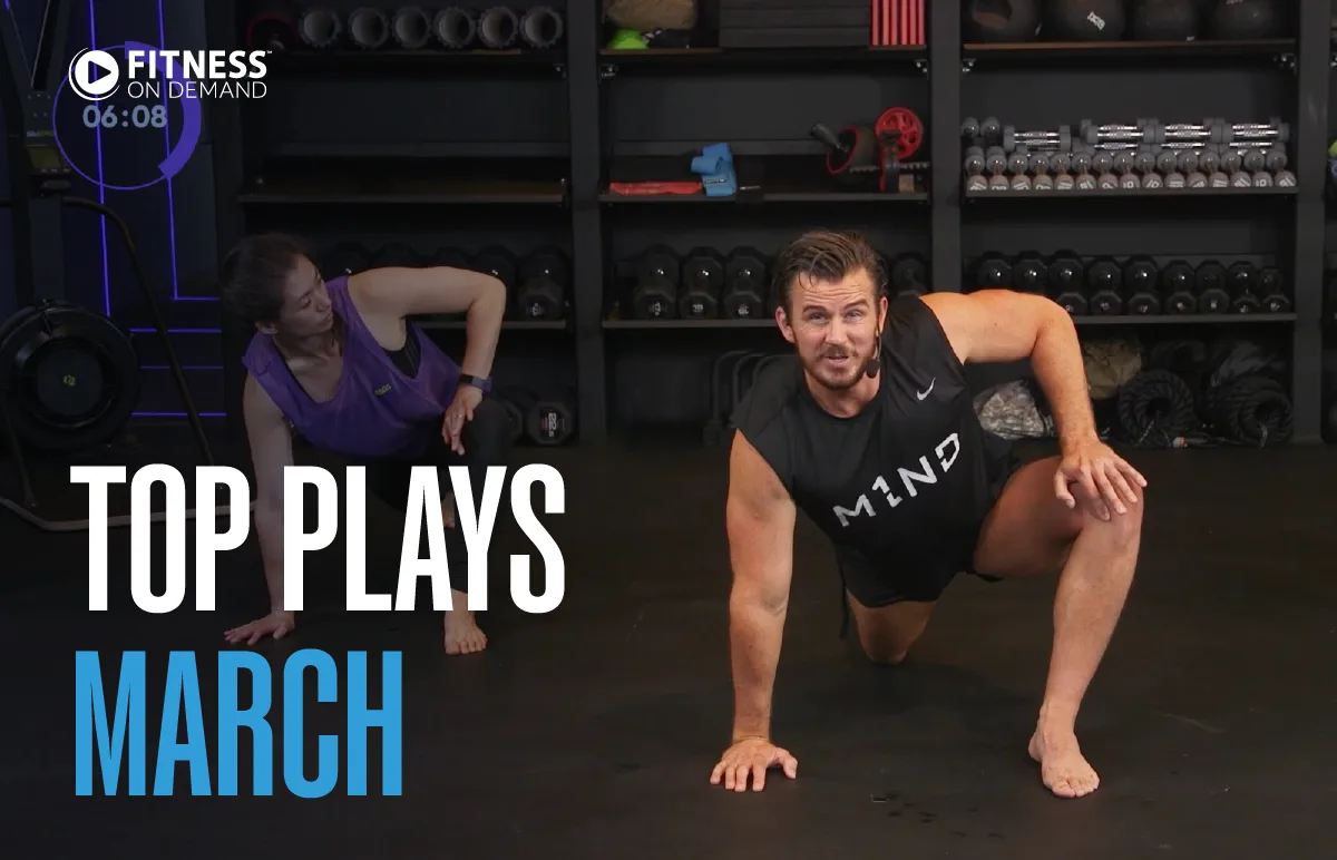 Two people exercise in a gym, one in a plank position and the other on one knee. Text reads Top Plays March and Fitness on Demand. Dumbbells and kettlebells are organized on shelves in the background.