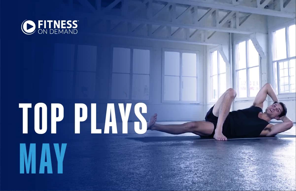 A man exercises on a yoga mat in a bright, spacious studio. Text on the left reads “Fitness On Demand. Top Plays May” in bold white and blue letters.