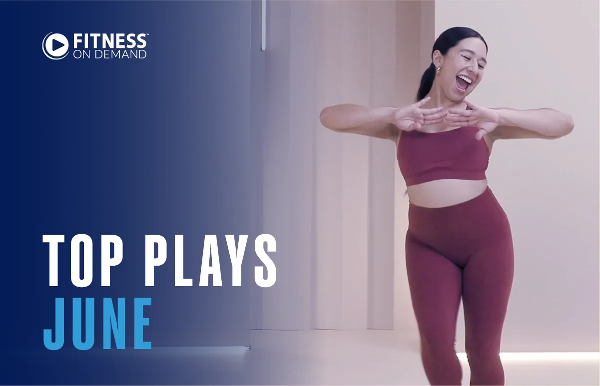 A smiling woman in a red workout outfit dances energetically indoors. Text on the left reads Fitness On Demand. Top Plays June. Background is a modern, light-colored studio.