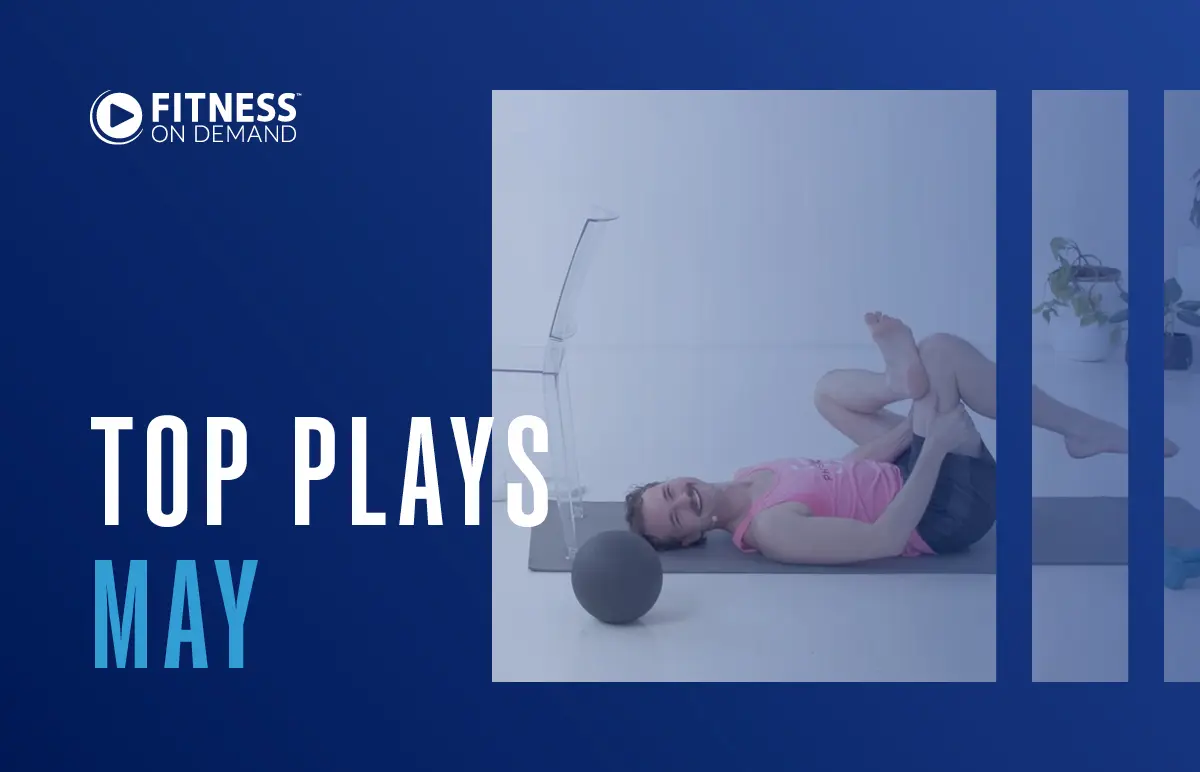 A person in workout clothes stretches on a yoga mat next to an exercise ball. Text on the image reads Fitness On Demand and Top Plays May on a blue background.