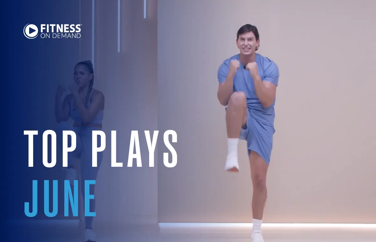 A man in blue workout clothes does a fitness routine in a studio. A woman in athletic gear exercises in the background. Text reads: “Fitness on Demand. Top Plays June.”.