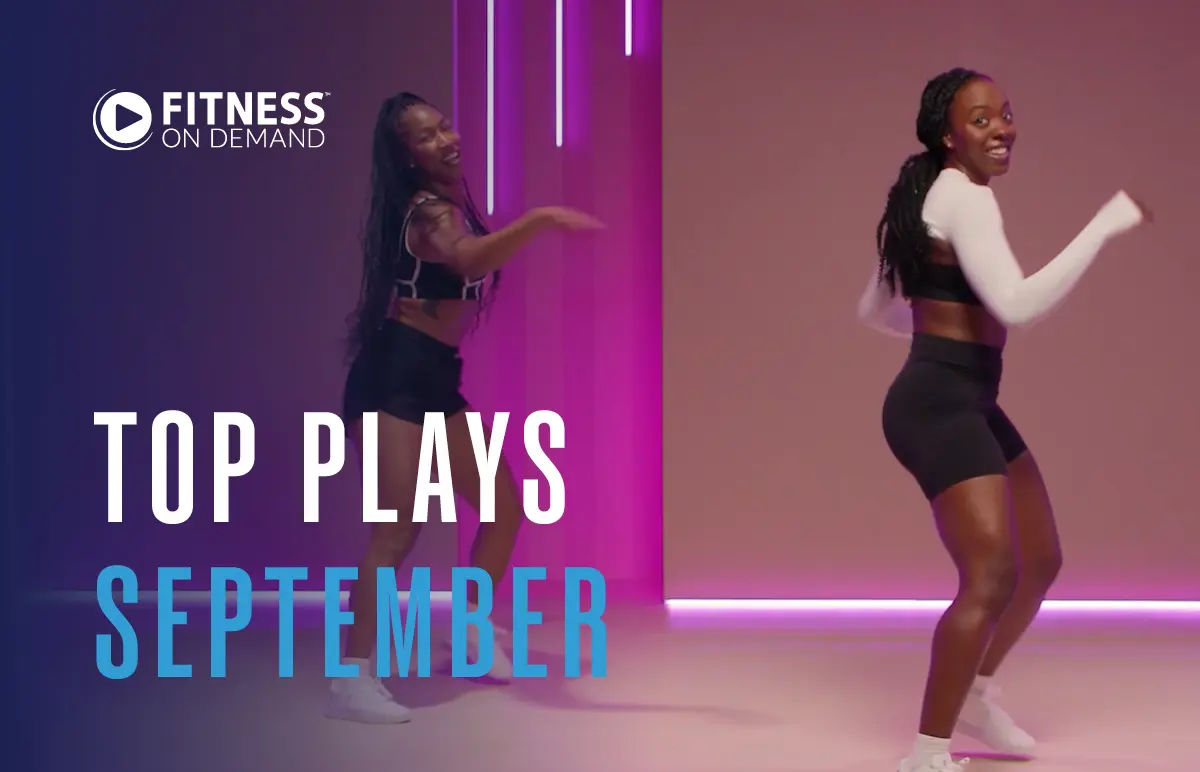 Two women in athletic wear dance and smile in a brightly lit studio with pink and purple lights. Text reads Fitness On Demand Top Plays September.