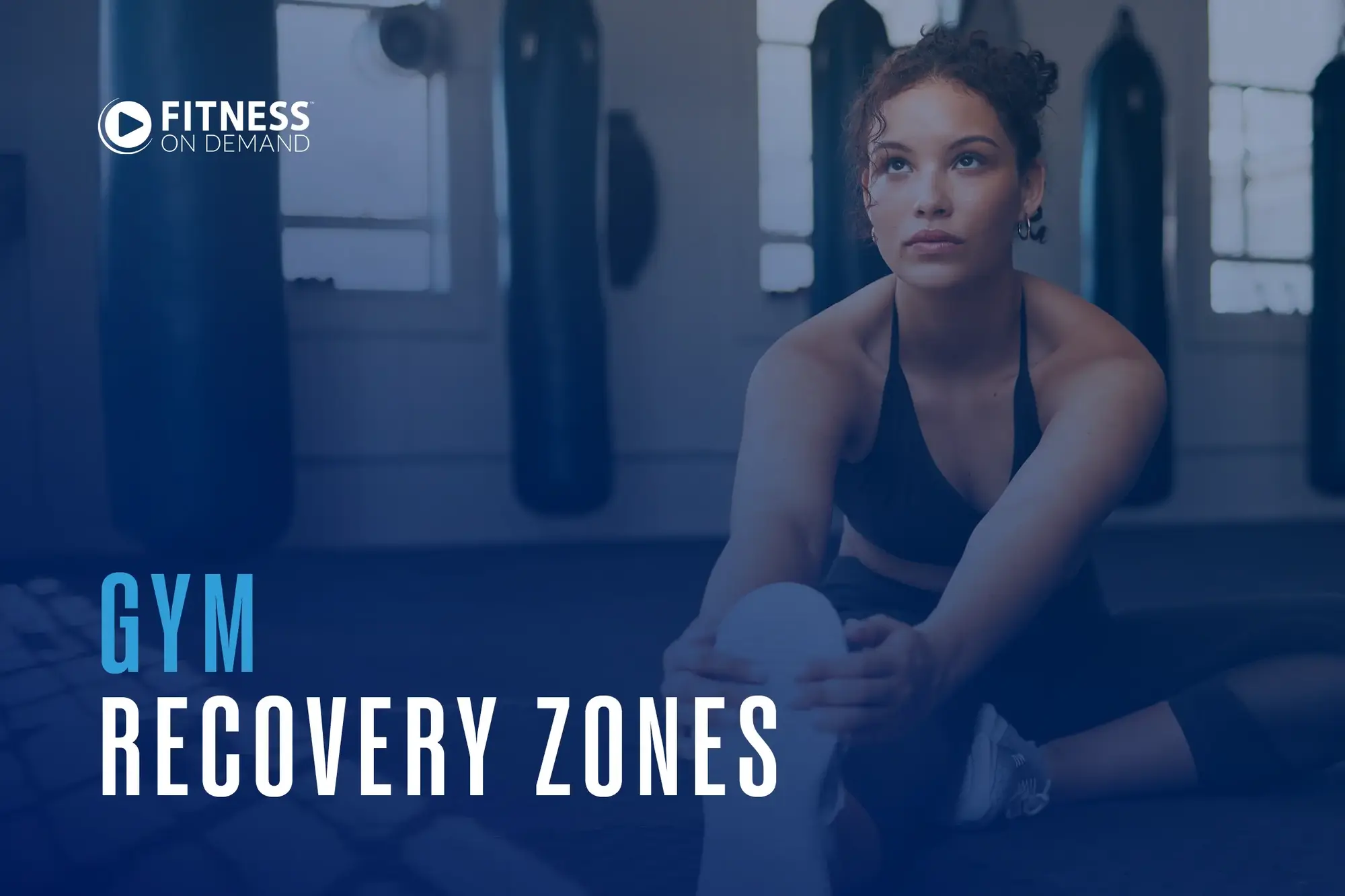 A woman in athletic wear stretches on a gym floor with punching bags in the background. Text reads Fitness On Demand. Gym Recovery Zones.