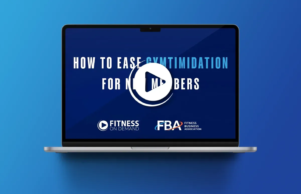A laptop displaying a blue screen with the text How to ease gymtimidation for new members and logos for Fitness On Demand and the Fitness Business Association. A white play button icon is centered on the screen.