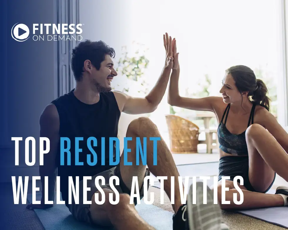 A man and woman in workout clothes sit on exercise mats indoors, smiling and giving each other a high five. Text reads: Fitness On Demand Top Resident Wellness Activities.