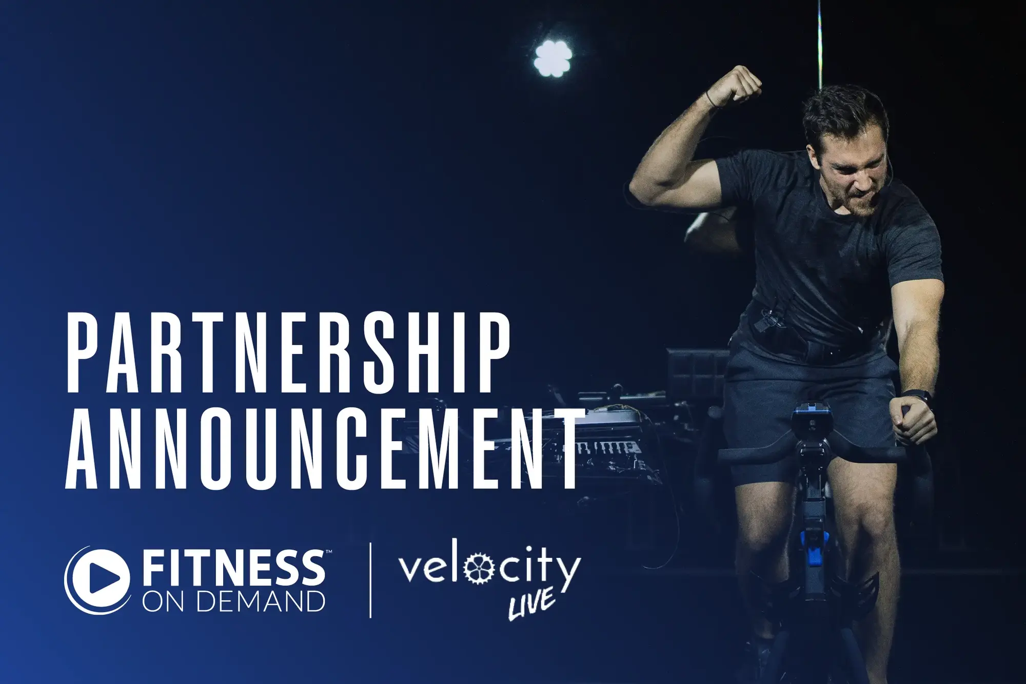 A man rides an exercise bike and flexes his arm on a dark stage. Large text reads “Partnership Announcement.” Logos for Fitness On Demand and Velocity Live are displayed at the bottom.