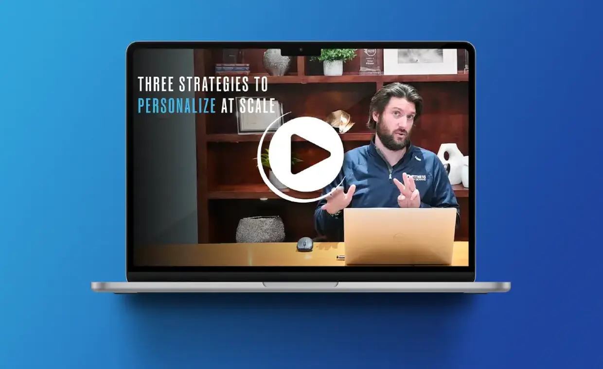 A laptop displays a paused video webinar with text: "Three Strategies to Personalize at Scale," featuring a Marketing Director, Nick Gustafson, gesturing while speaking, with shelves and decor visible behind him on a wooden background.