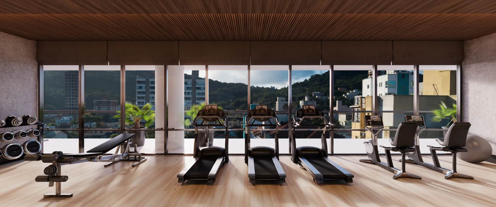 A modern gym with treadmills, exercise bikes, and weights faces large windows that offer a city and mountain view. The space has wooden floors and a wooden ceiling, with natural light filling the room.